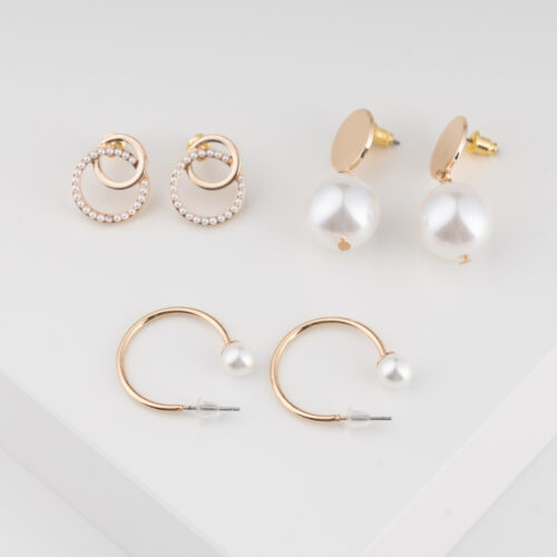 Ein Set von Trisa Accessoires an zierlichen Ohrringen und goldigem Modeschmuck mit weissen Perlen vor weissem Hintergrund.