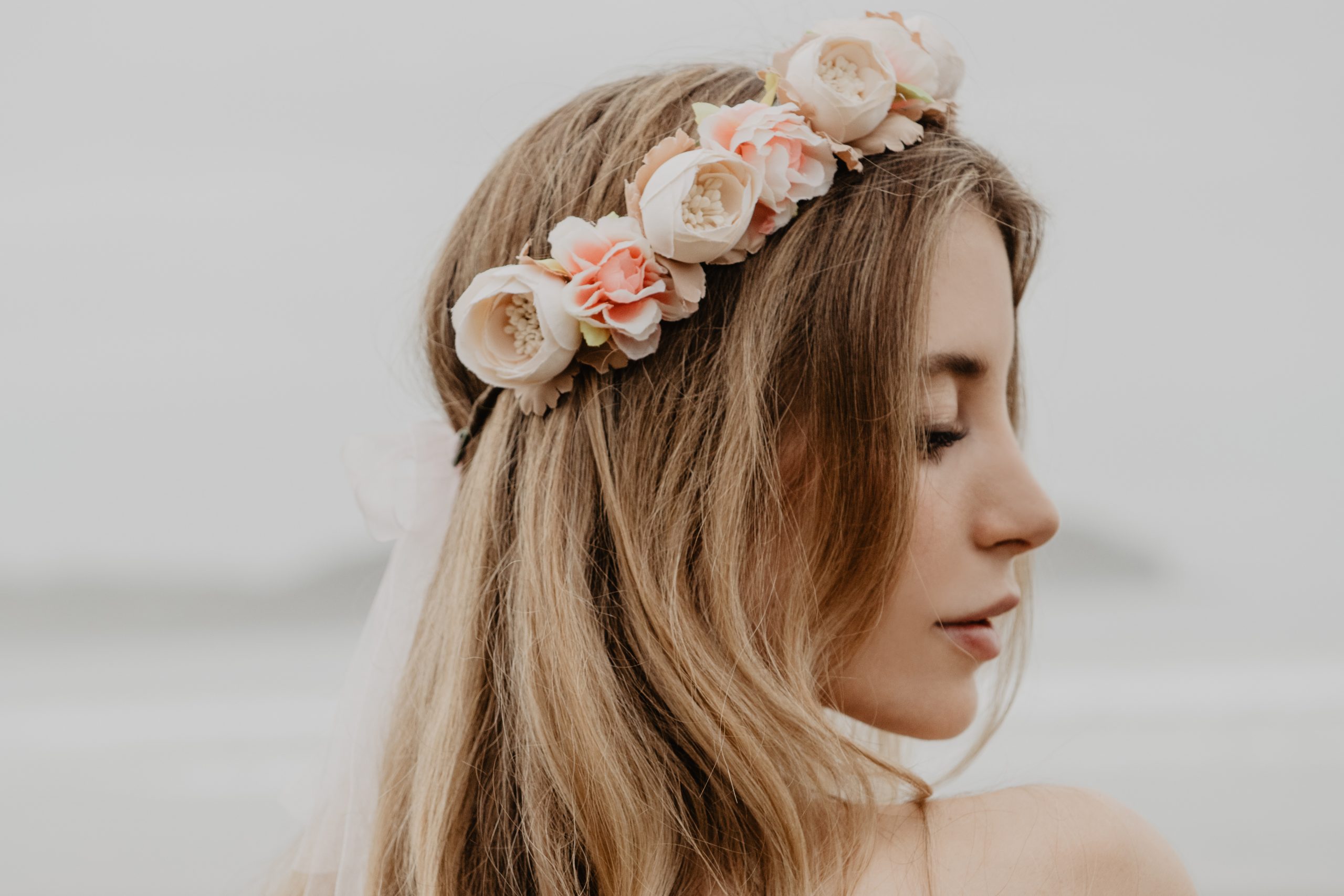 Verträumte junge Frau mit blonden Haaren trägt einen romantischen Blumenkranz im Haar von CELEBRIDE Trisa Accessoires, am Strand in Ibiza