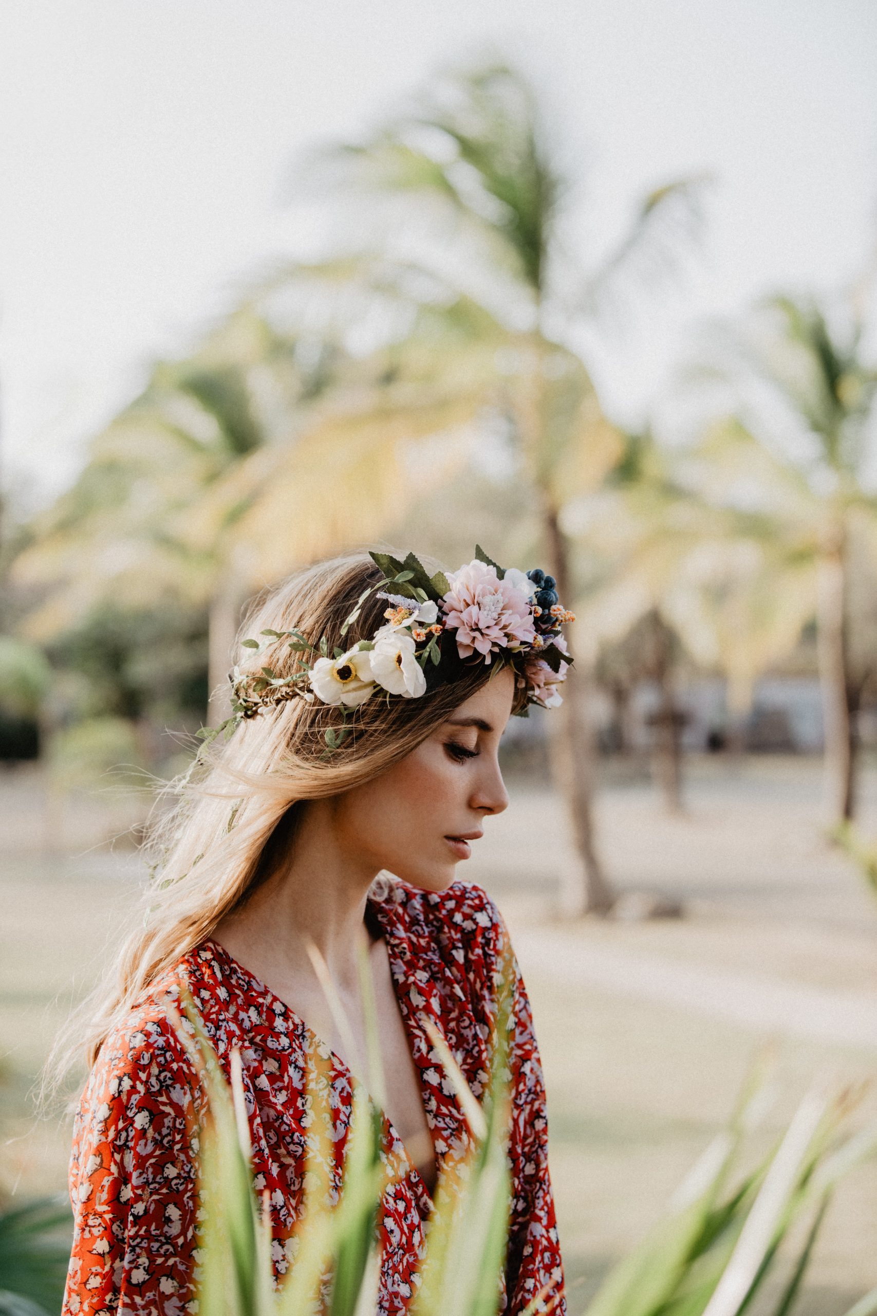 Eine junge Frau mit Blumenkranz von CELEBRIDE Trisa Accessoires, spaziert am Sand Strand von Panama, mit Palmen im Hintergrund.