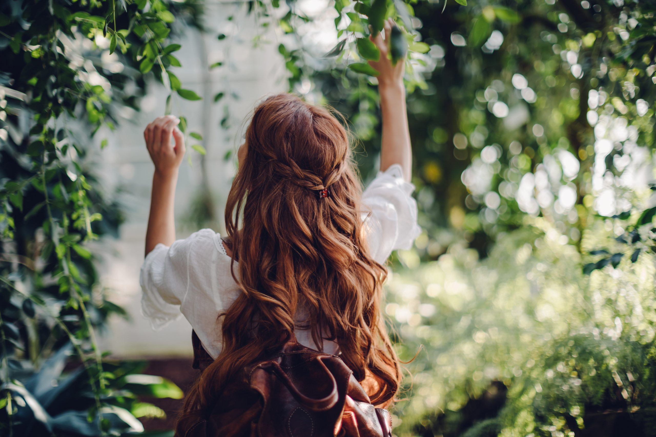 Eine junge Frau in der Natur, mit brünetten langen Locken, trägt Rucksack von Trisa Accessoires und Nachhaltigkeit ist ihr wichtig