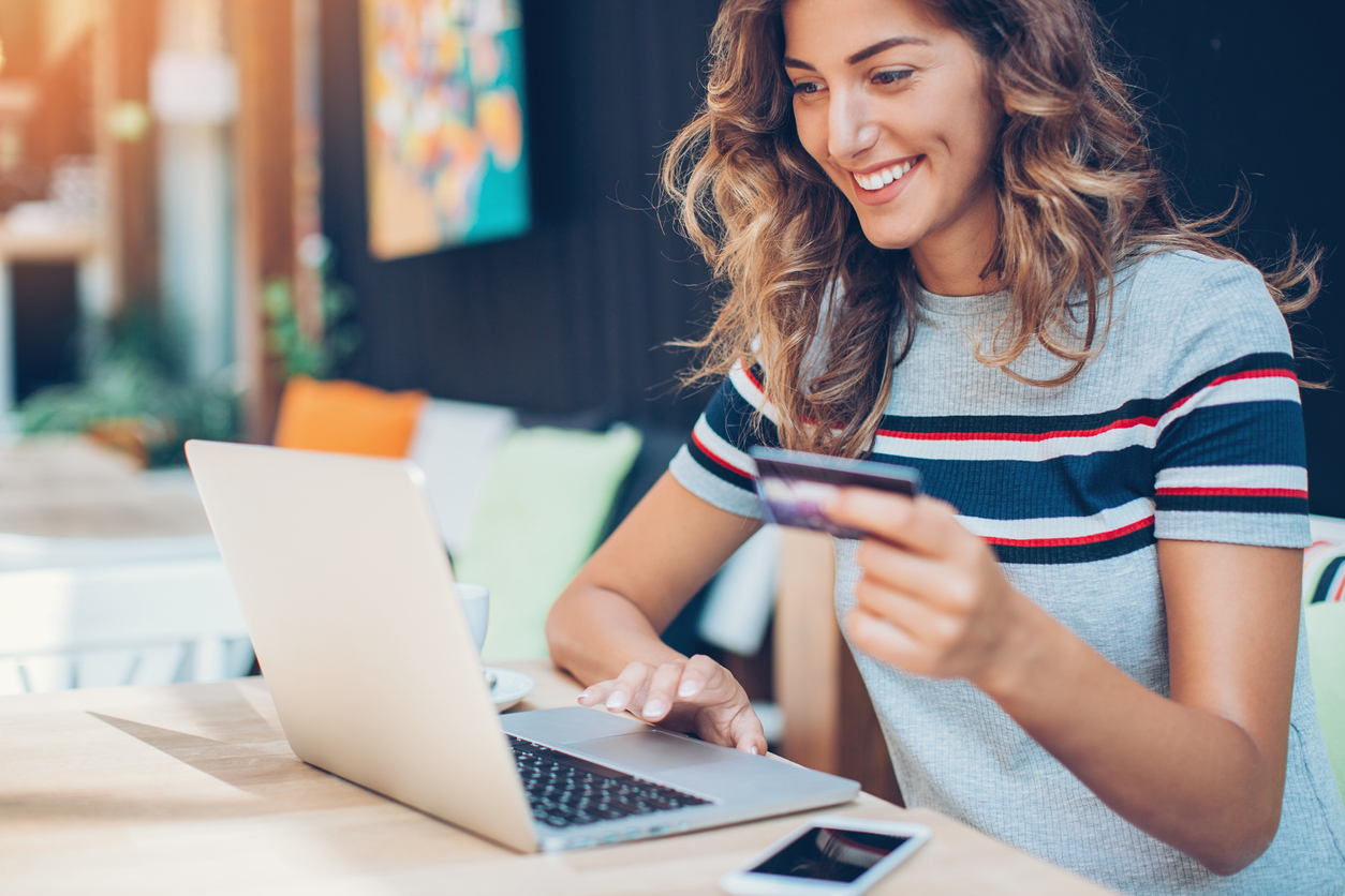 eine junge Frau mit lockigem Haar, blickt in ihren Laptop, sitzt im Cafe, kauft Haarschmuck auf dem Online Shop von Trisa Accessoires ein.