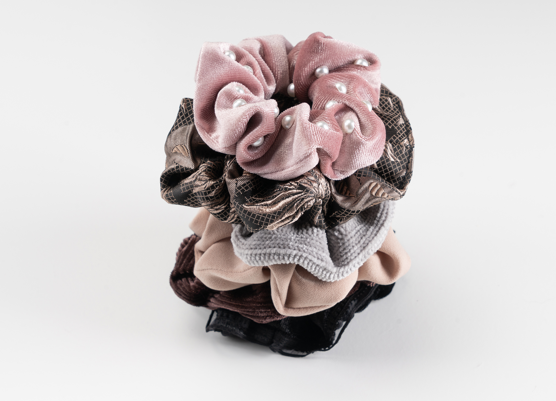 Ein dekoratives Set an Haarschmuck Scrunchies von Trisa Accessoires, in den Farben schwarz, grau, rosa und braun, platziert auf weissem Hintergrund.