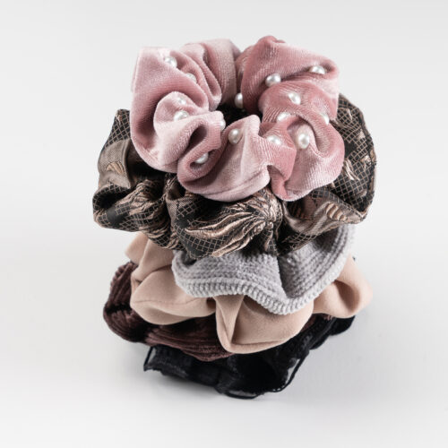 Ein dekoratives Set an Haarschmuck Scrunchies von Trisa Accessoires, in den Farben schwarz, grau, rosa und braun, platziert auf weissem Hintergrund.
